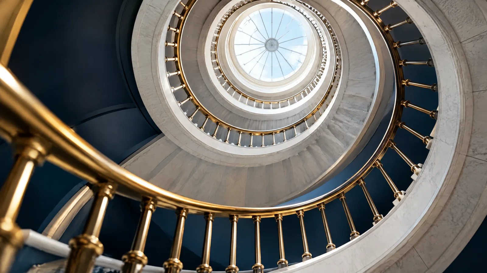 Looking up through a spiral staircase rising towards a bright skylight, representing continuous improvement of risk management